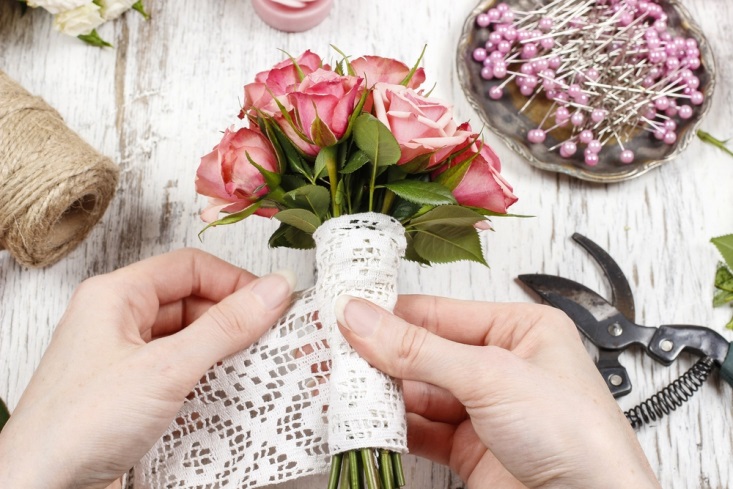 Florist wrapping a small bouquet of pink roses with lace