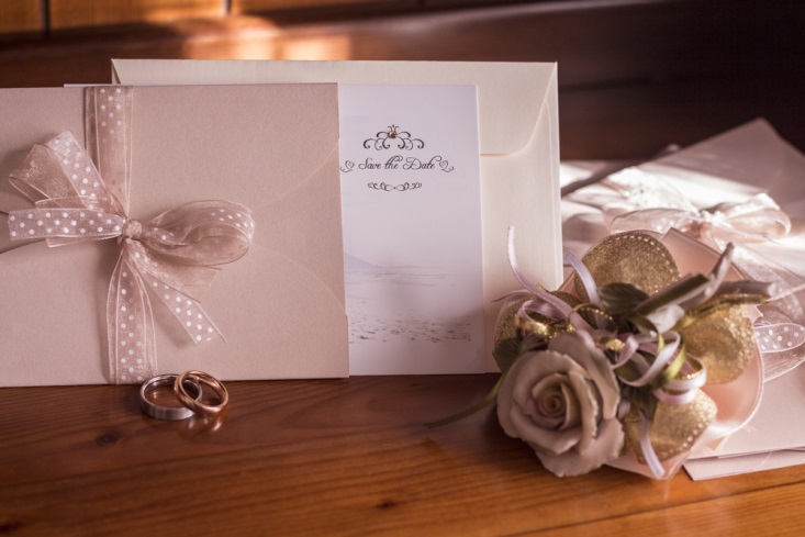 Taupe save-the-date cards, two wedding bands, and a bouquet of flowers