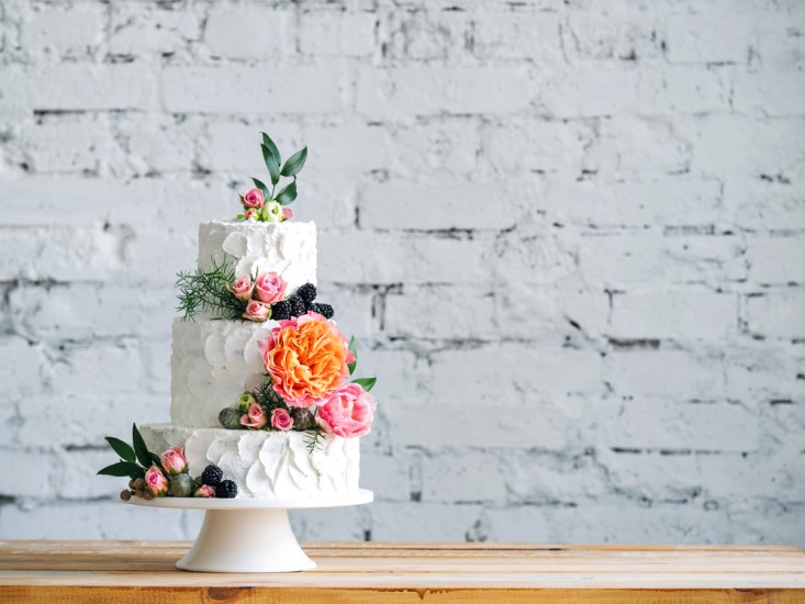 Wedding cake on wooden table in front of white-washed brick wall