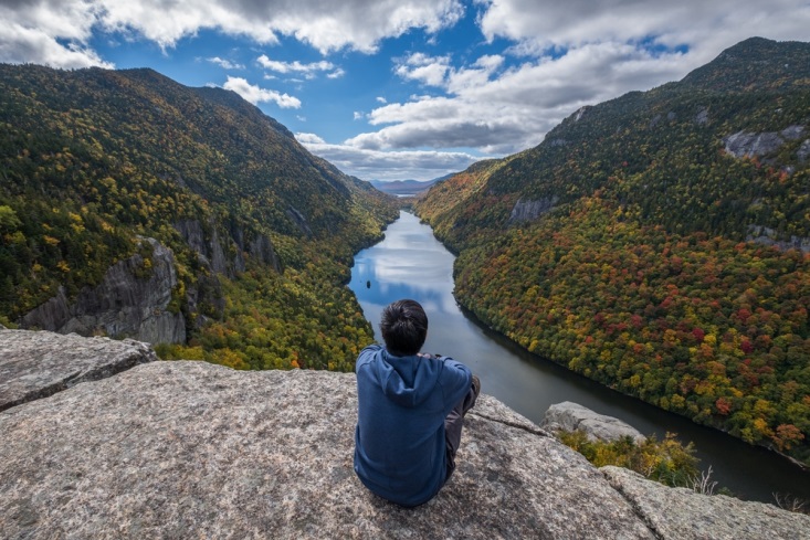 Man sitting on edge of cliff and surveying the breathtaking views of the Adirondacks in New York