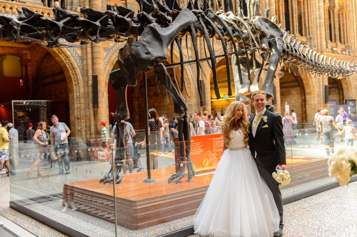 Newly married couple posing in front of dinosour fossil at their museum wedding