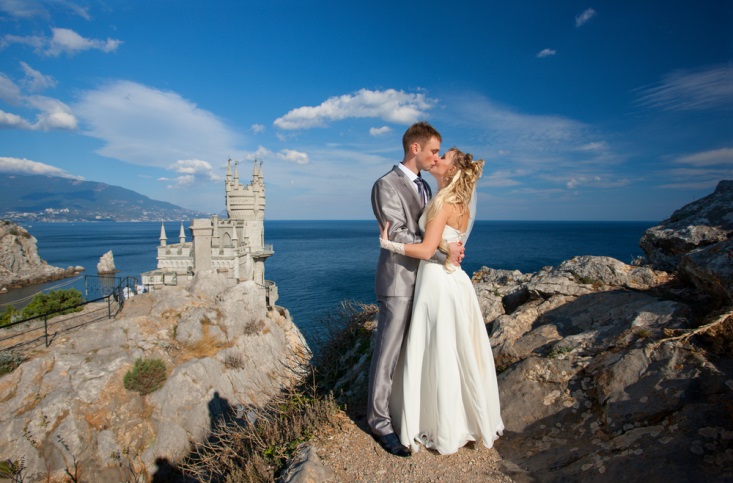 Newly married couple kissing at their outdoor venue by a castle on the coast