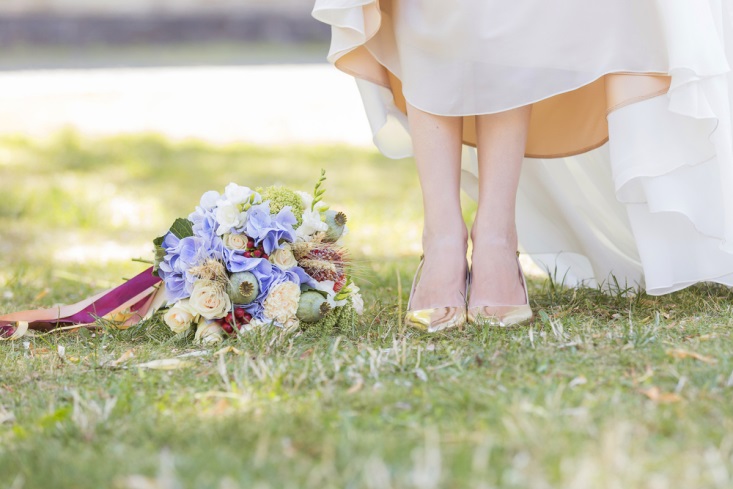 Bride holding up her dress to show off her shoes next to her bouquet